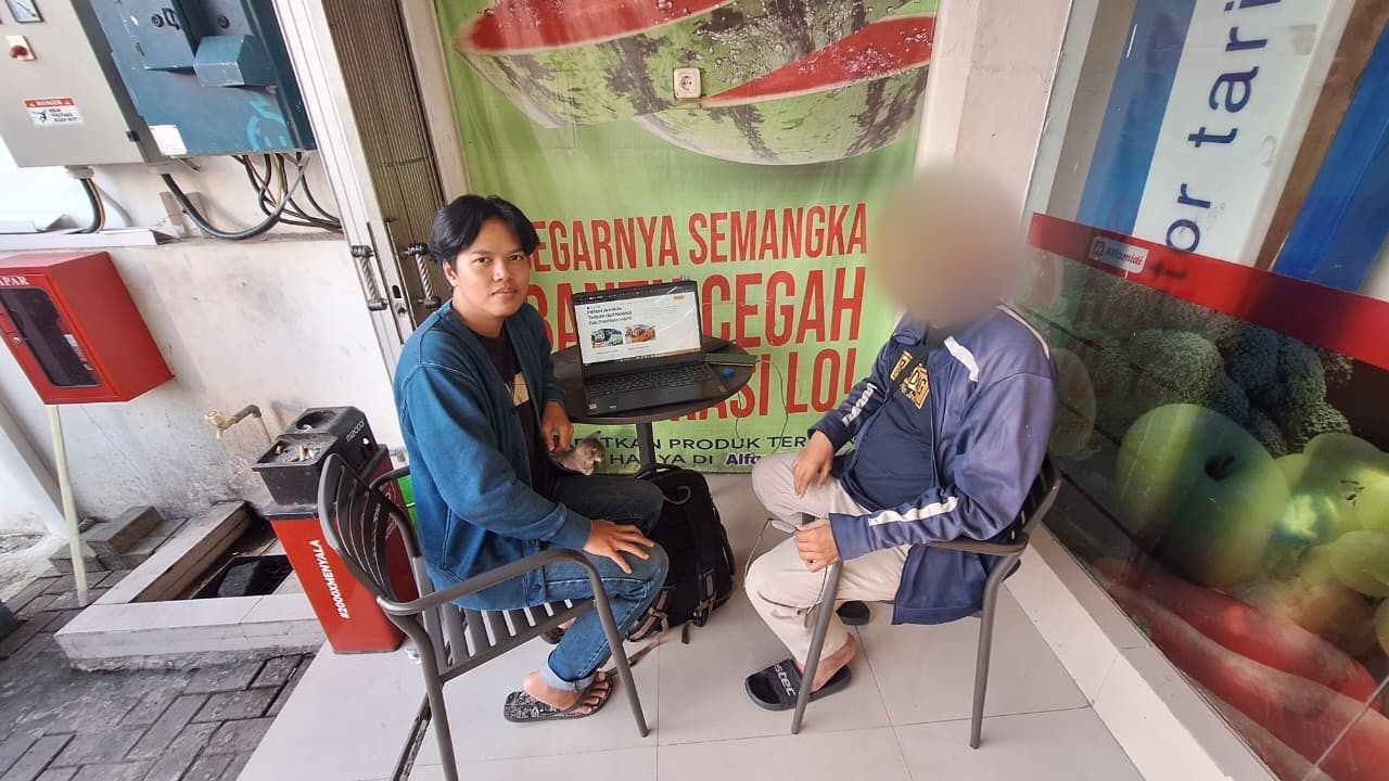 Fadal duduk bersama klien Deny Trans di depan minimarket, dengan laptop yang menampilkan website di meja. Wajah klien diburamkan.